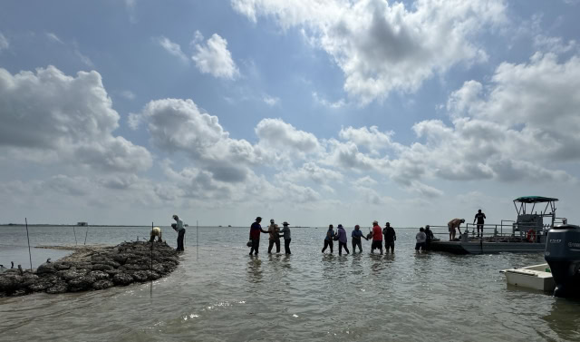 A line of volunteers moving bags of oyster shell from a barge to a small shell island.