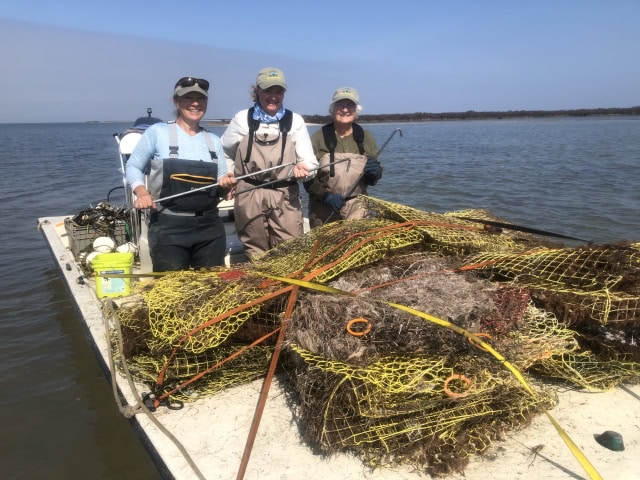 Three women on a boat with metal hooks and a pile of crushed crab traps.