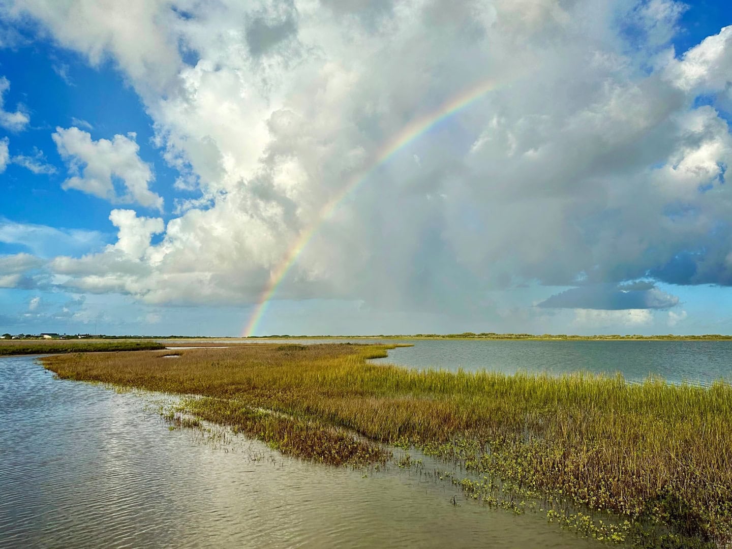 Rainbow touching the ground in the distance beyond an estuary.